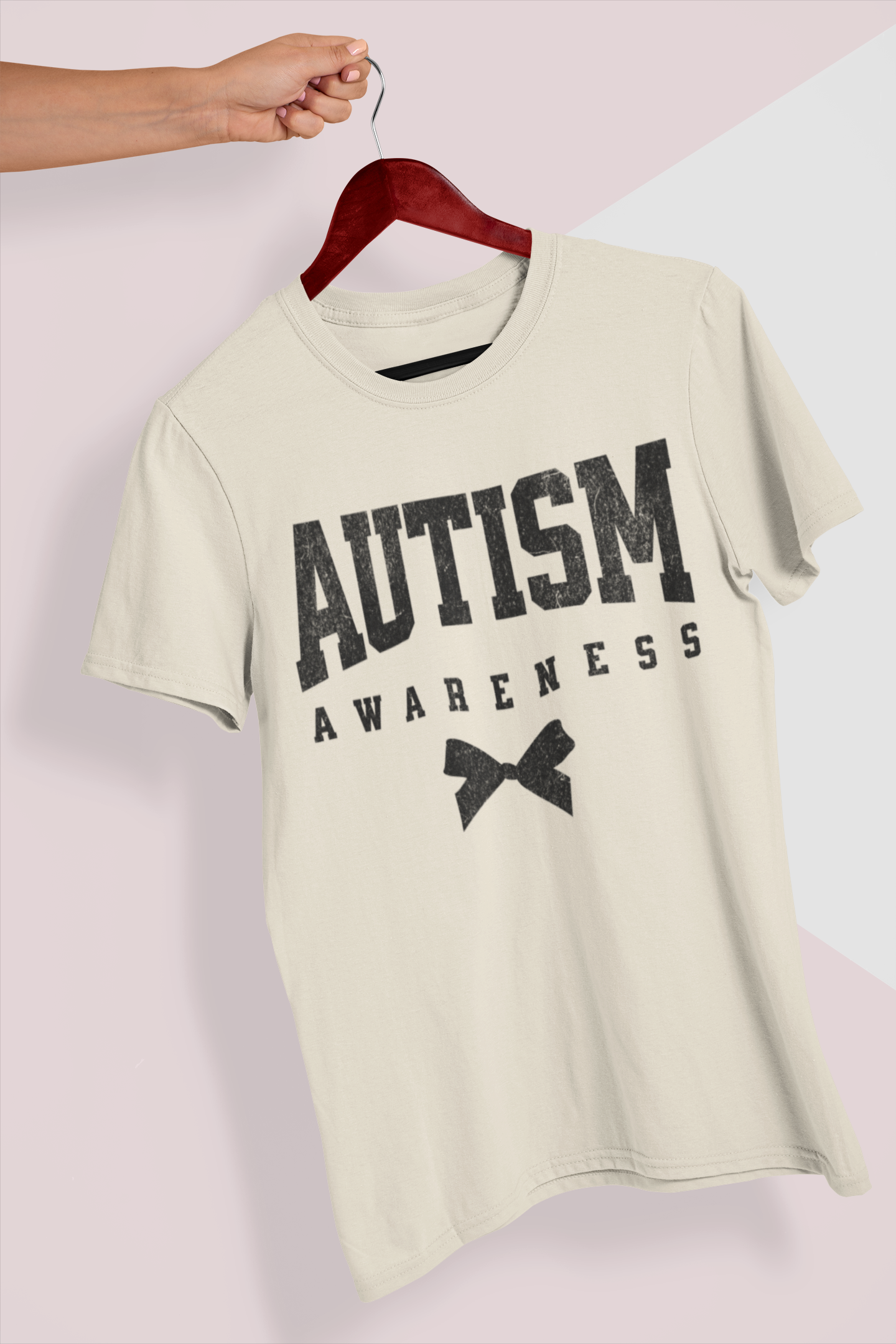 A person holding a beige T-shirt on a hanger that says "Autism Awareness"