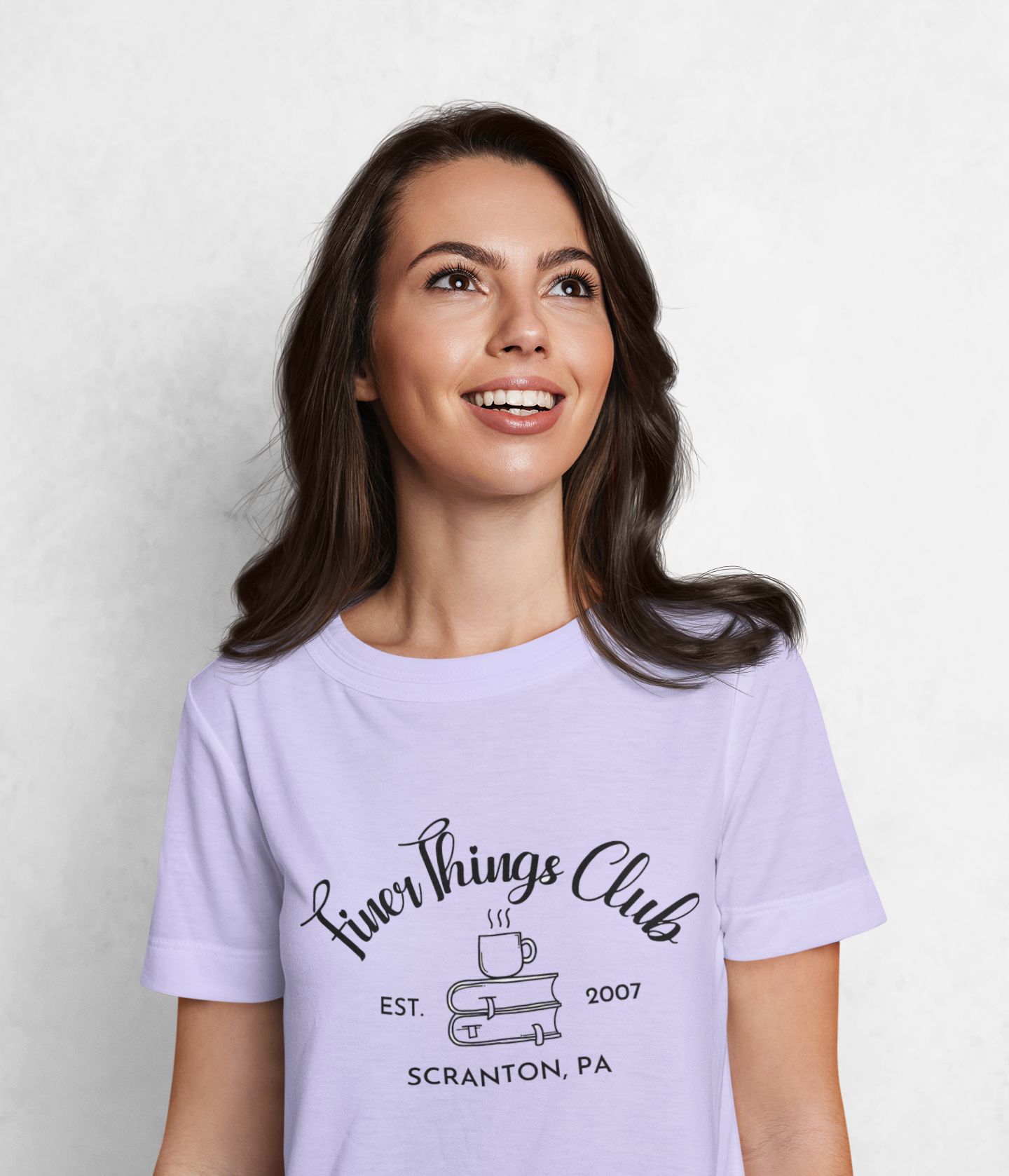A girl smiling while wearing a T-Shirt that says "Finer Things Club" with coffee and books on it