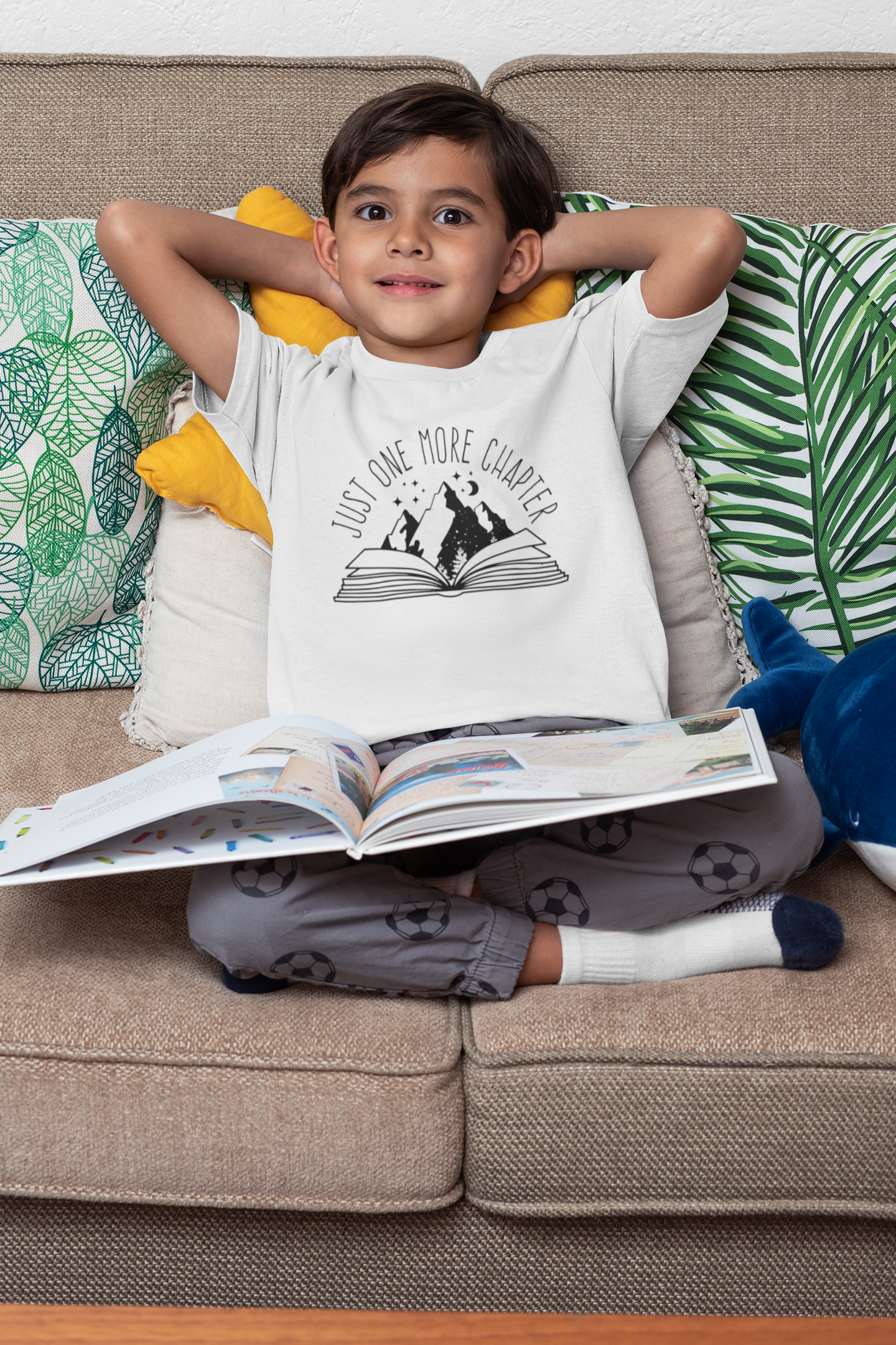 A little boy reading a book with a T-shirt that says "Just One More Chapter"