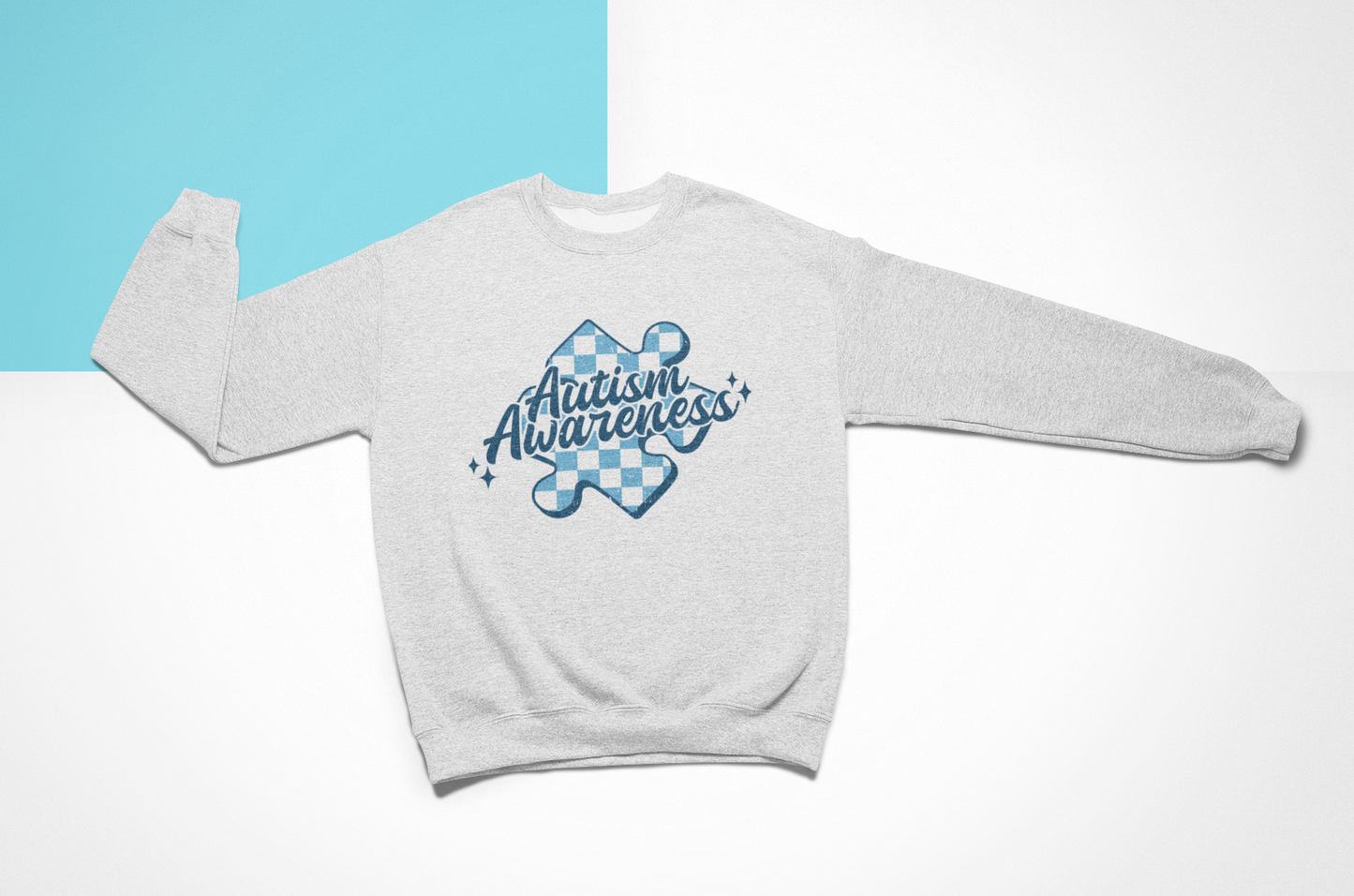 A heather grey sweatshirt that says "autism Awareness" on it with a blue checkered puzzle piece behind the quote. 