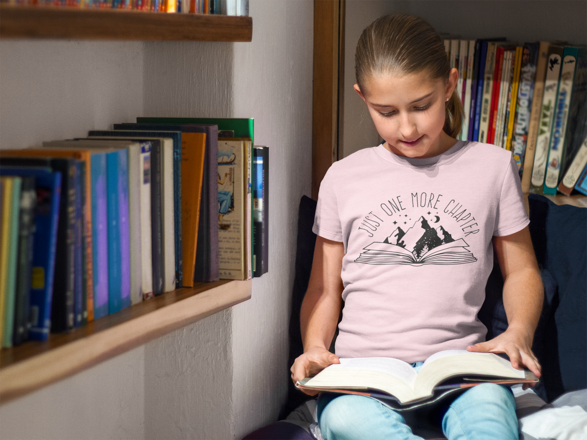 A little girl reading a book with a T-shirt that says "Just One More Chapter"