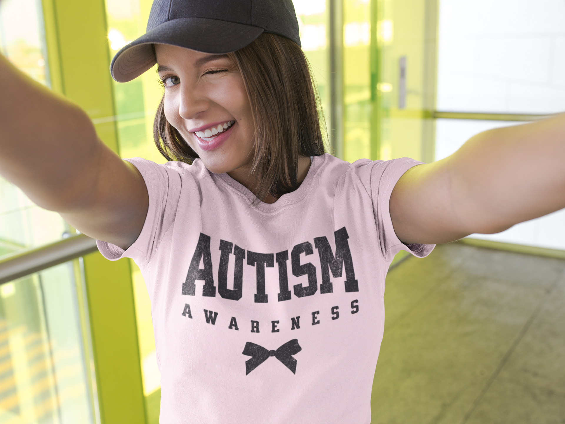 A girl taking a selfie wearing a hat and a pink Autism Awareness T-Shirt