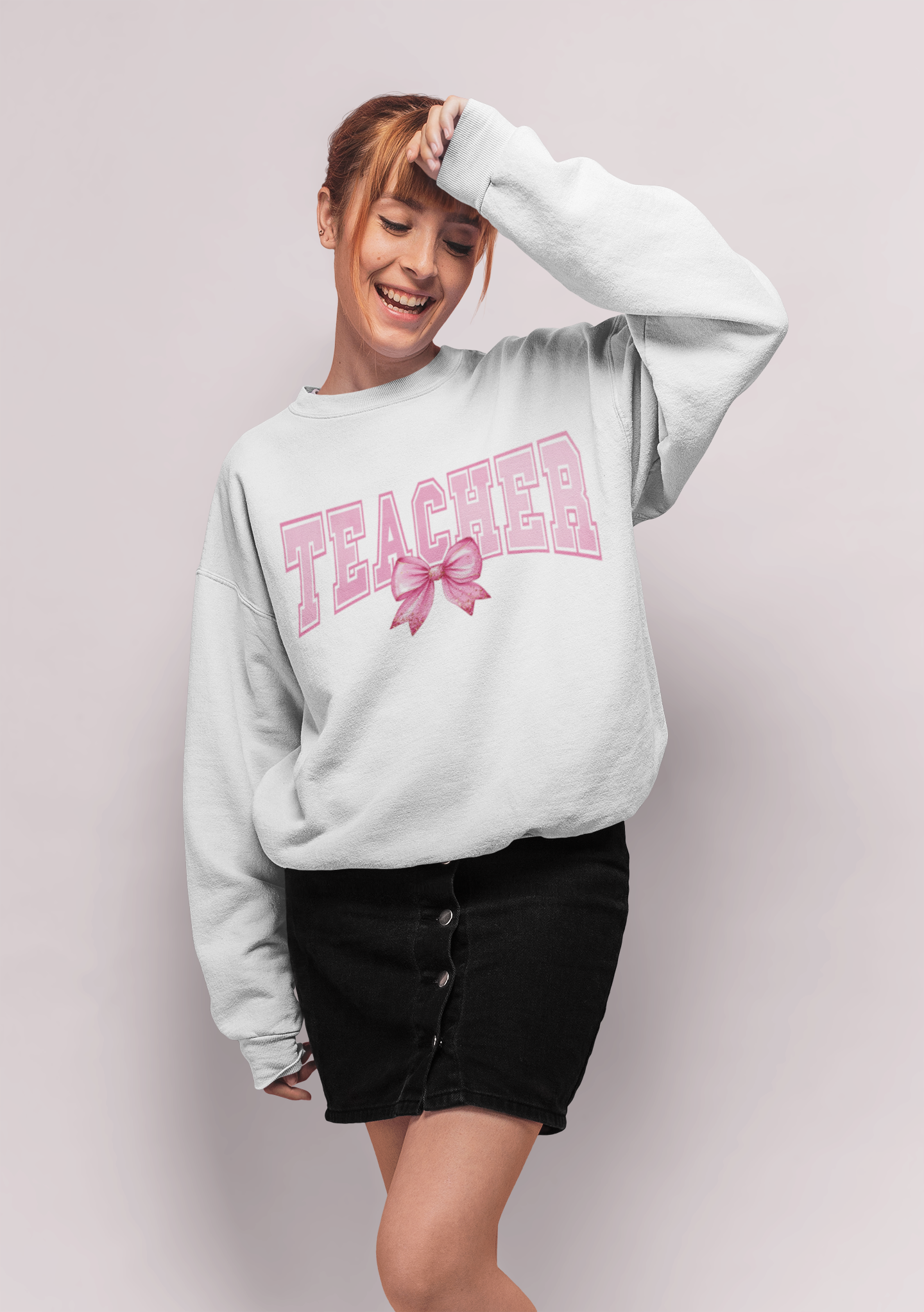 A girl wearing a white sweatshirt that says Teacher with a bow